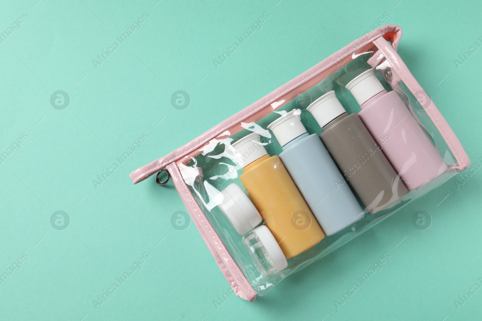 Photo of Cosmetic travel kit in plastic bag on turquoise background, top view. Space for text