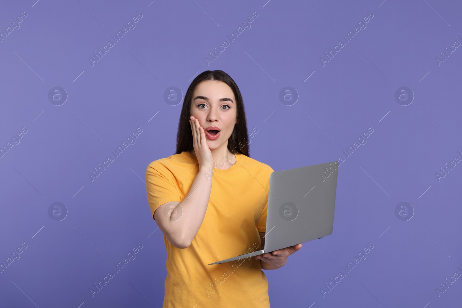 Photo of Surprised young woman with laptop on lilac background