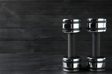 Photo of Two metal dumbbells on black wooden table. Space for text