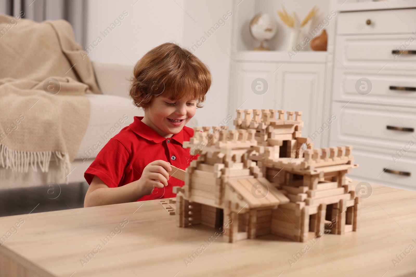 Photo of Cute little boy playing with wooden castle at table in room. Child's toy