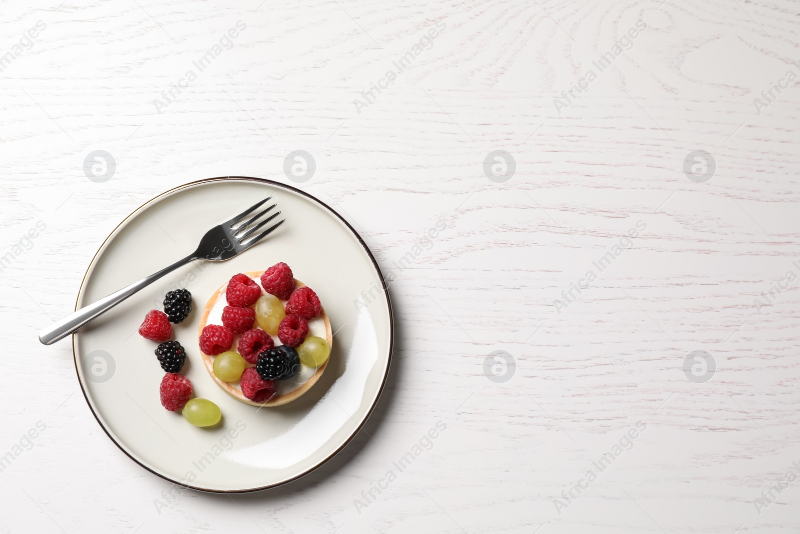Photo of Delicious tartlet with berries on white wooden table, top view. Space for text