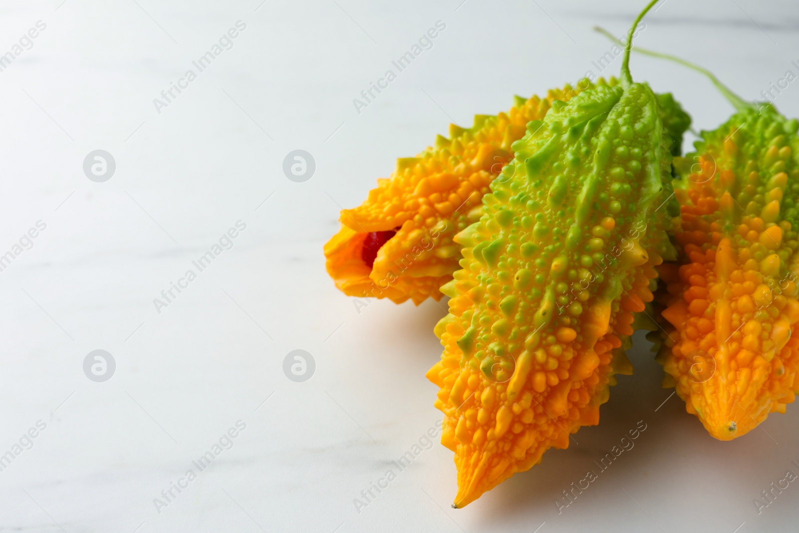 Photo of Bitter melons on white marble table, closeup. Space for text