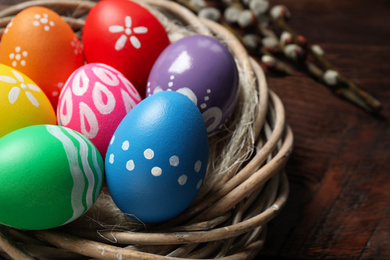 Photo of Colorful Easter eggs in decorative nest on wooden background, closeup