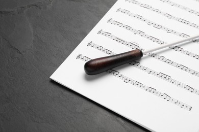 Photo of Conductor's baton and sheet music on black background, closeup view