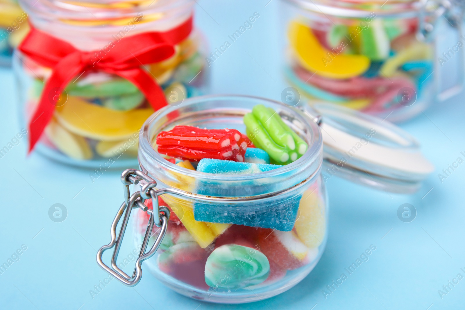 Photo of Tasty colorful jelly candies in glass jars on light blue table, closeup