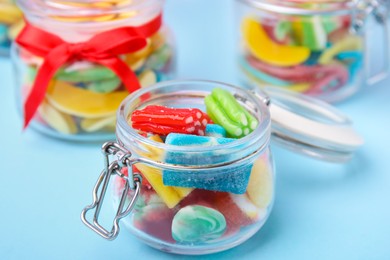 Tasty colorful jelly candies in glass jars on light blue table, closeup