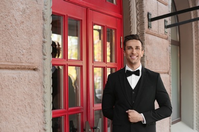 Photo of Young doorman in elegant suit standing near restaurant entrance