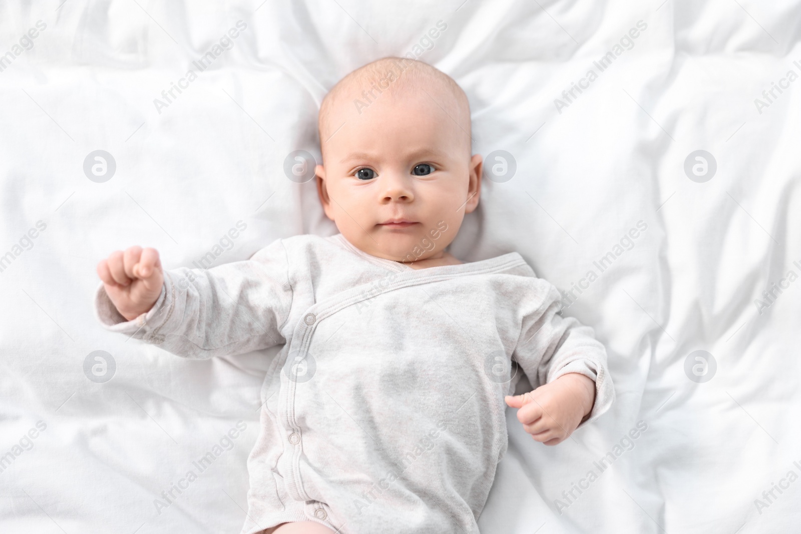 Photo of Cute little baby lying on white sheets, top view