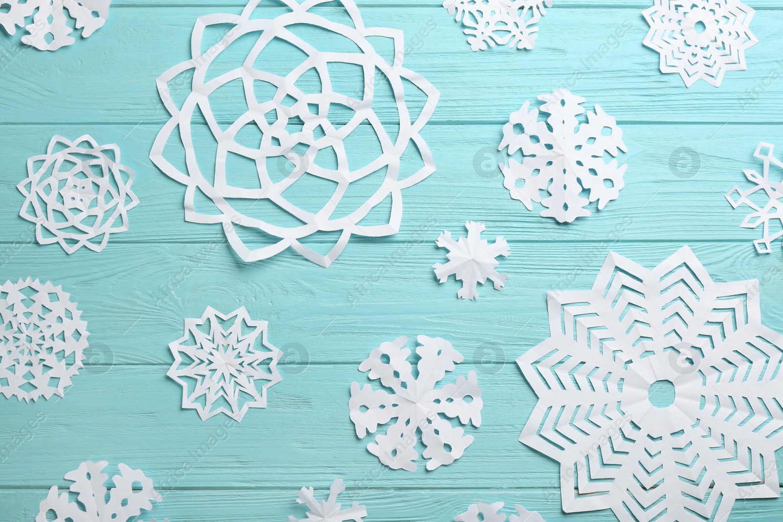 Photo of Many paper snowflakes on turquoise wooden background, flat lay