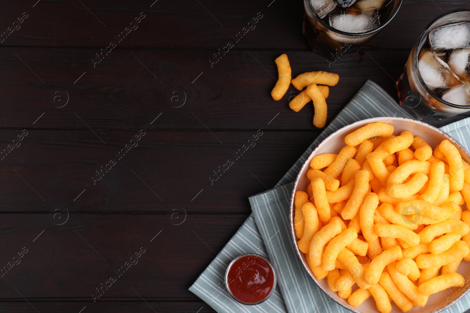 Photo of Crunchy cheesy corn snack, ketchup and refreshing drink on wooden table, flat lay. Space for text