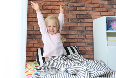 Photo of Cute little girl stretching after sleeping in bed at home