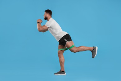 Photo of Young man exercising with elastic resistance band on light blue background