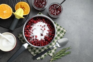 Photo of Making cranberry sauce. Fresh cranberries with sugar in saucepan and ingredients on gray table, flat lay. Space for text