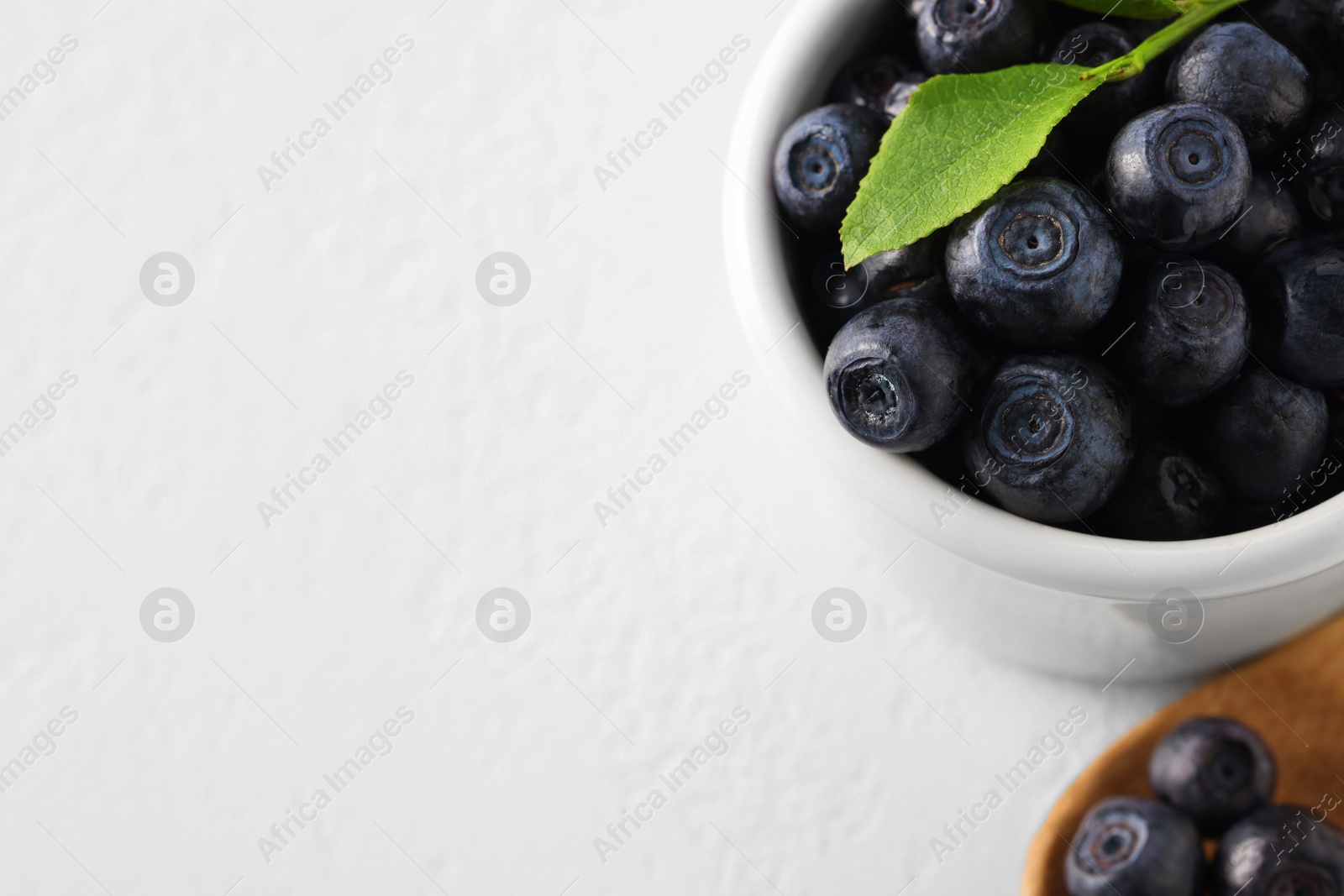 Photo of Ripe bilberries and leaf in bowl on white table, closeup. Space for text