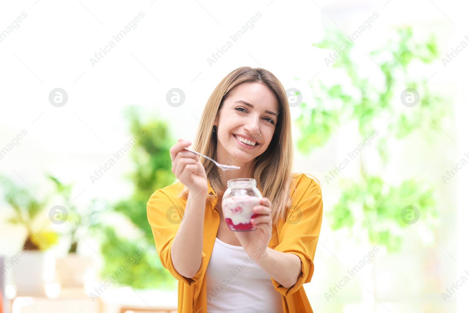 Photo of Young attractive woman eating tasty yogurt, indoors