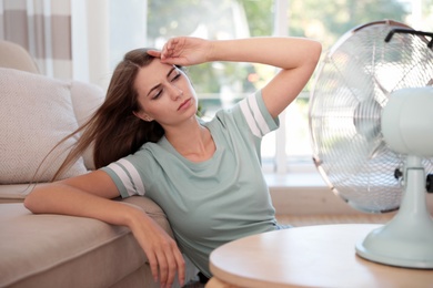 Photo of Woman enjoying air flow from fan in living room. Summer heat