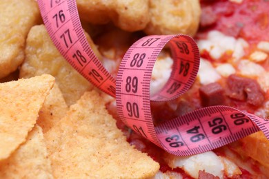 Photo of Chips, chicken nuggets, pizza with measuring tape as background. Diet concept