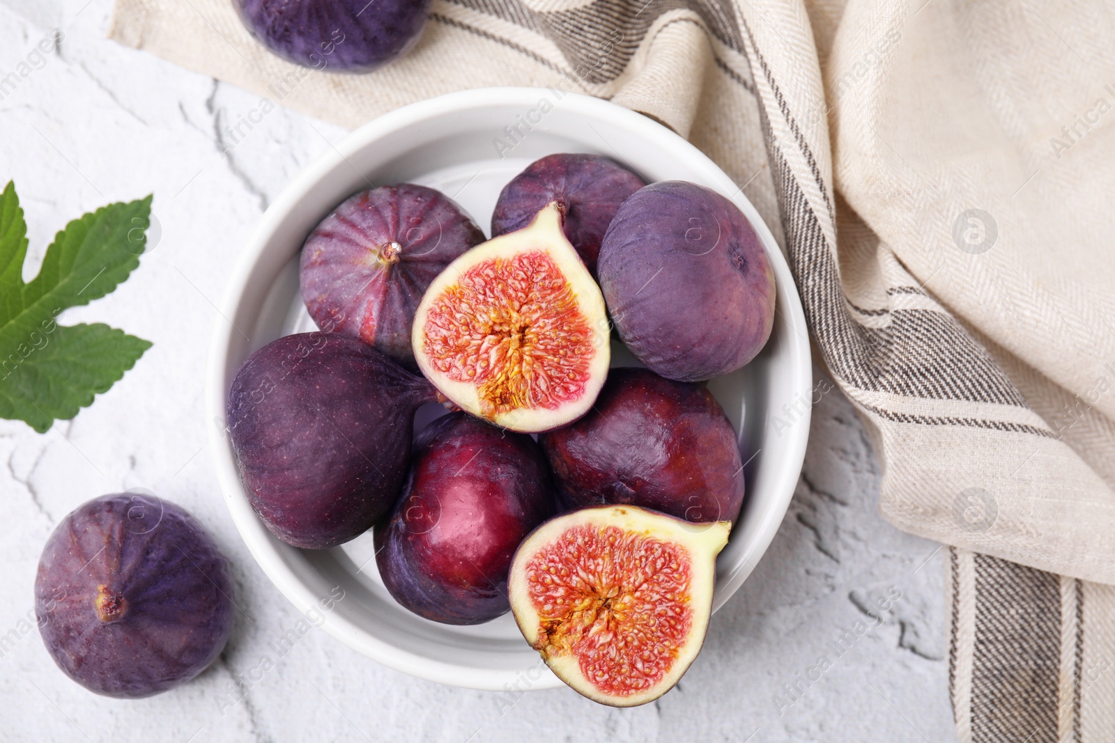 Photo of Bowl of tasty ripe figs on white textured table, flat lay