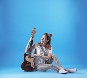 Young woman with electric guitar on color background