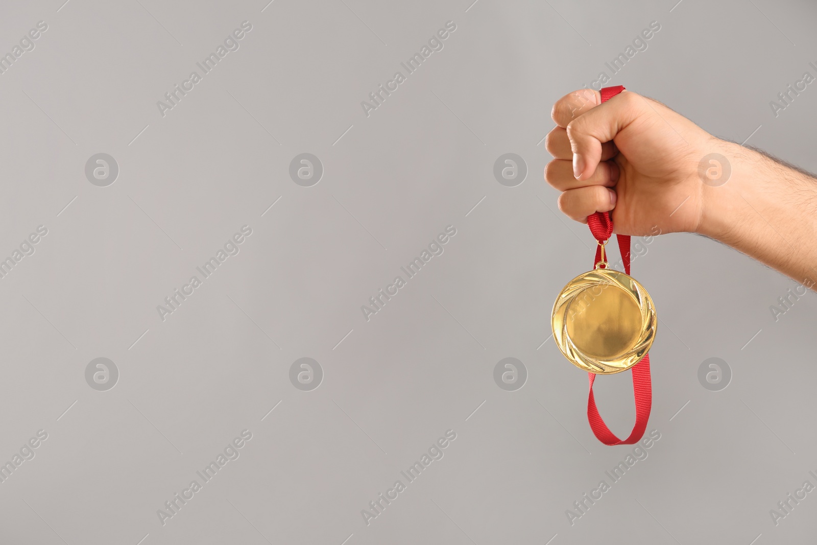 Photo of Man holding golden medal on grey background, closeup. Space for design