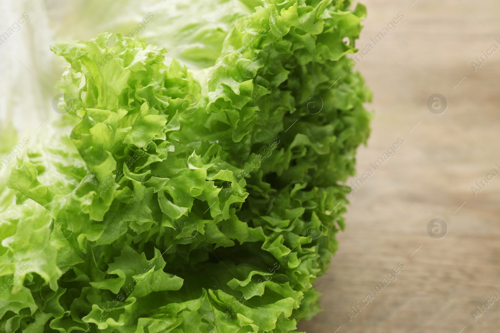 Photo of Fresh lettuce on wooden table, closeup. Salad greens