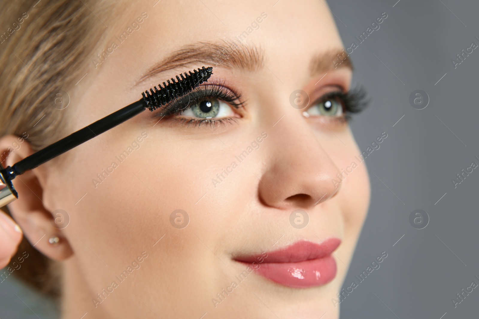 Photo of Beautiful woman applying mascara on light grey background. Stylish makeup