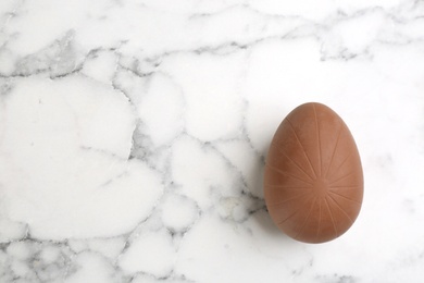 Photo of Sweet chocolate egg on white marble table, top view. Space for text