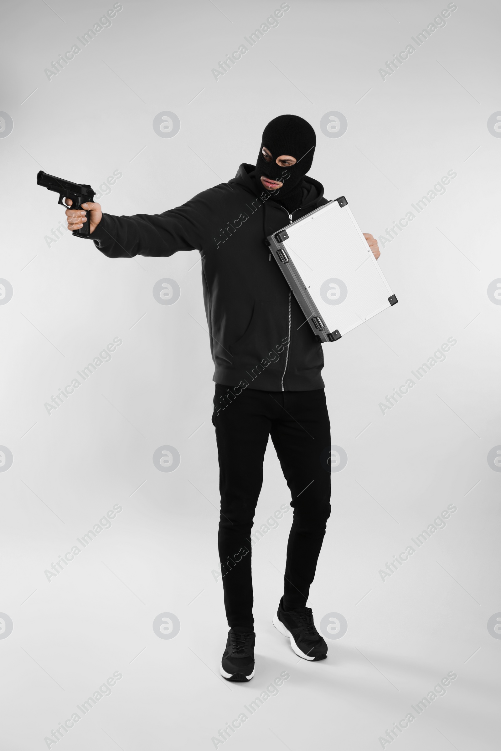 Photo of Man wearing black balaclava with metal briefcase and gun on light grey background