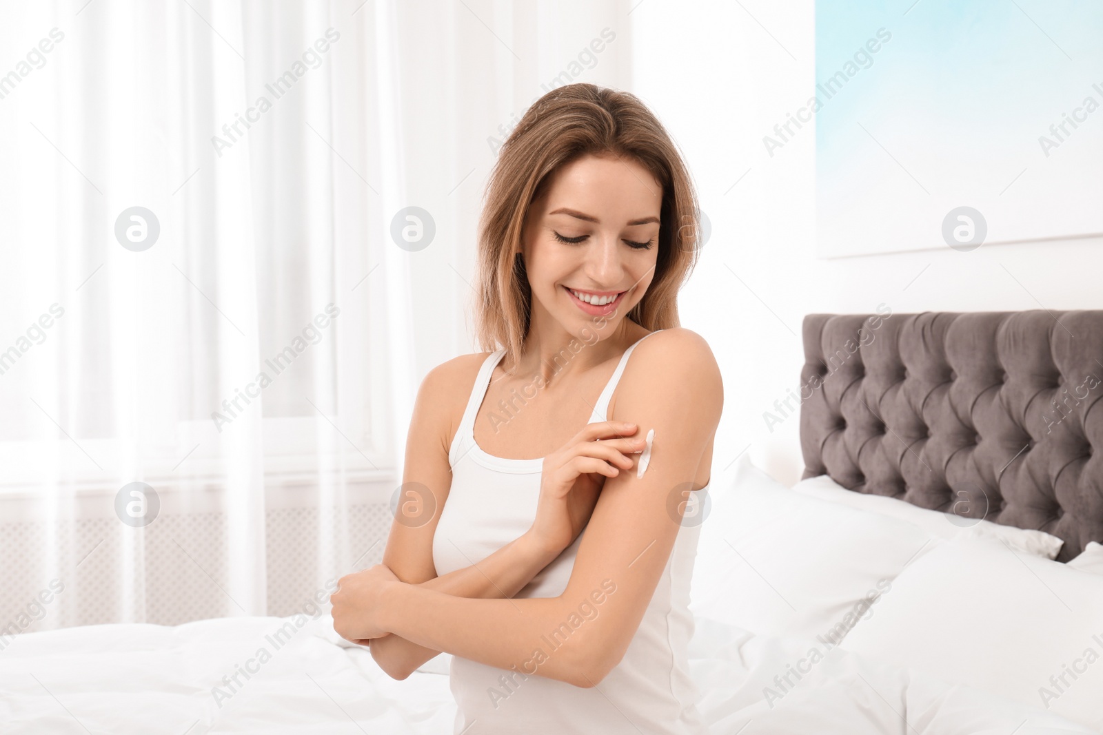 Photo of Young woman applying cream in bedroom. Beauty and body care