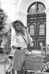 Beautiful woman with bicycle near ornate door on street, black and white effect