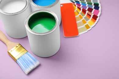 Open cans of paint with brush and palette on color background