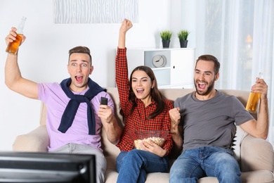 Photo of Young friends watching TV on sofa at home