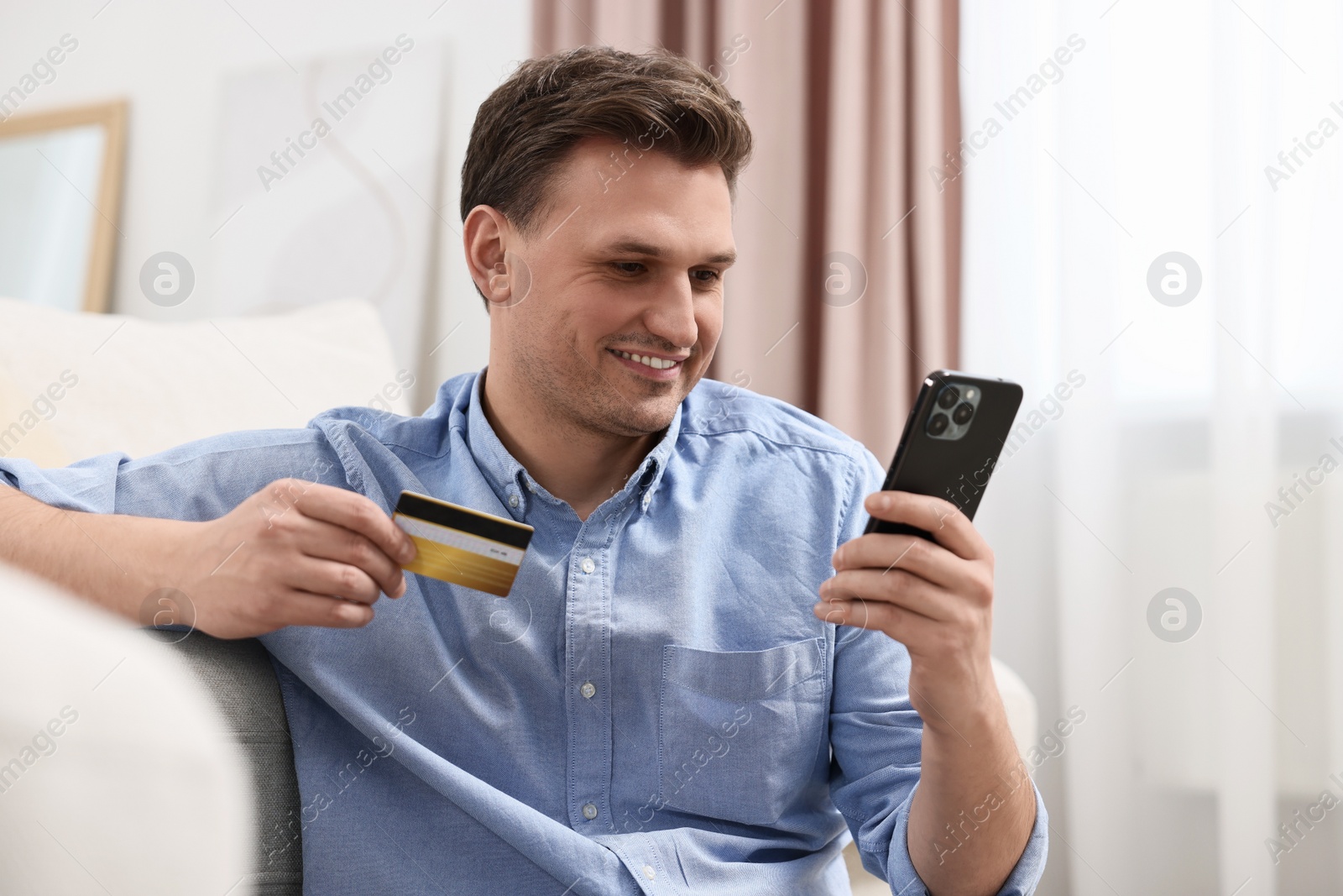 Photo of Happy man with credit card and smartphone shopping online at home