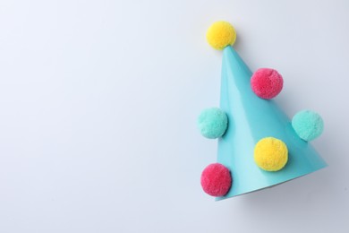 One blue party hat with pompoms on light background, top view. Space for text