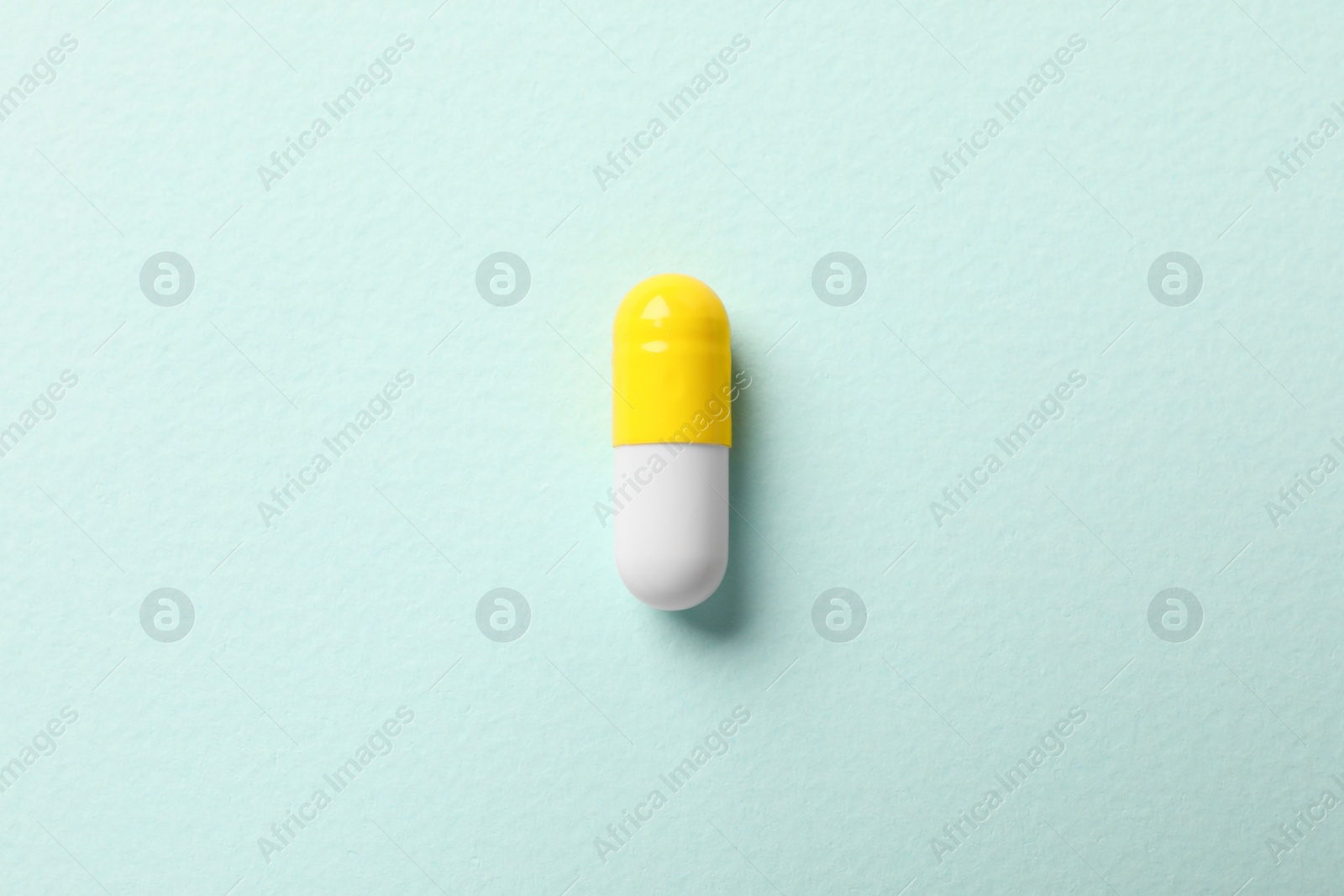 Photo of One colorful pill on mint background, top view