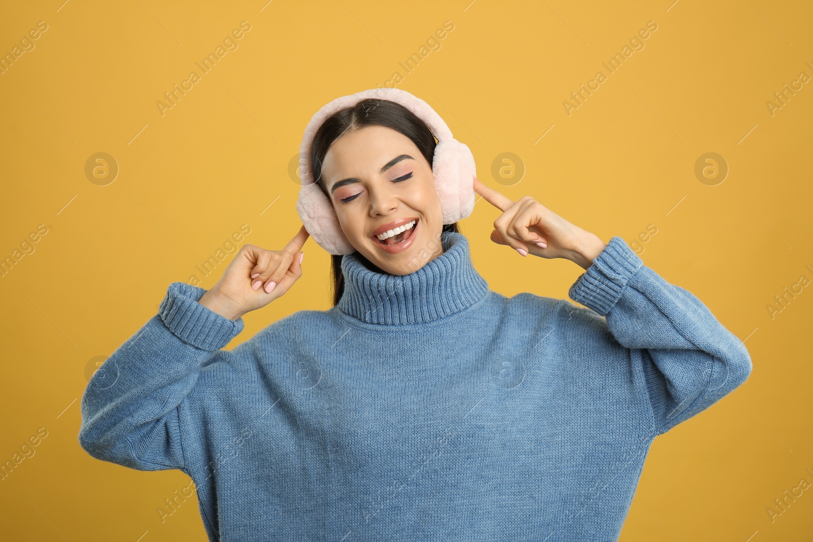 Photo of Beautiful young woman wearing earmuffs on yellow background