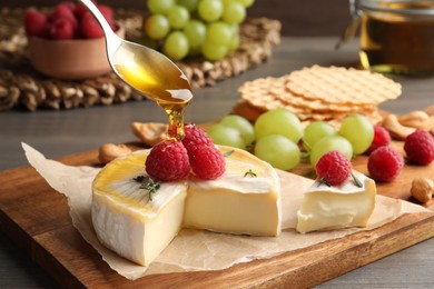 Photo of Pouring honey onto brie cheese served with raspberries on table, closeup