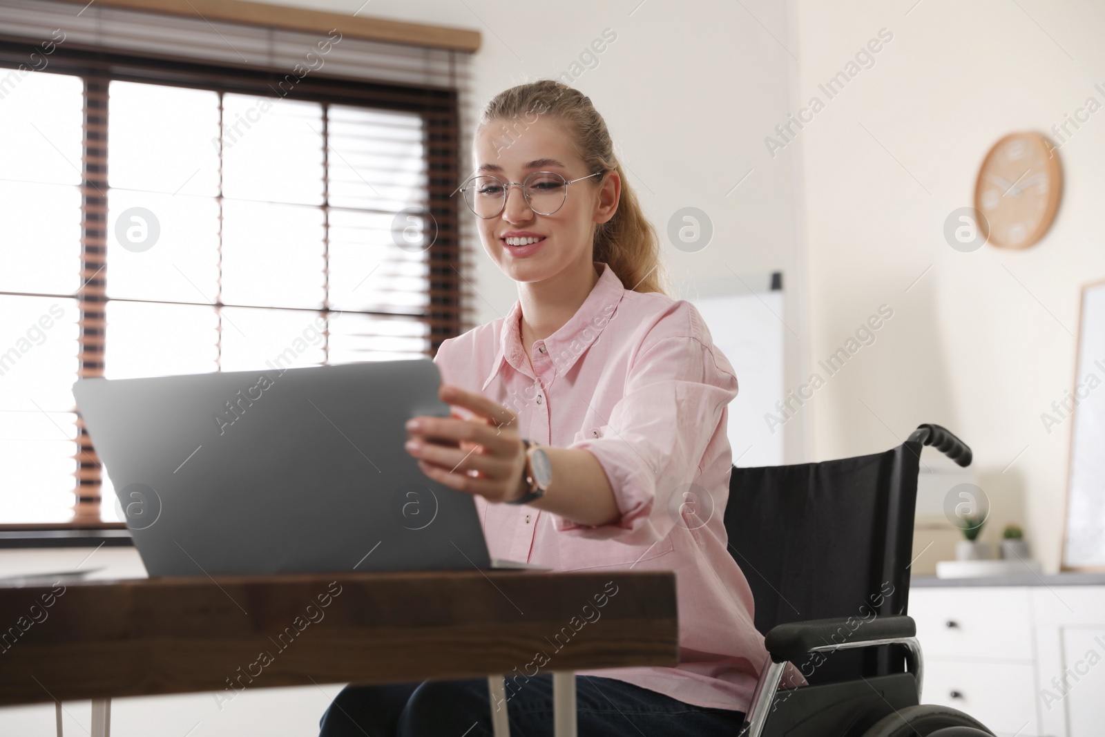 Photo of Portrait of woman in wheelchair working with laptop at table indoors