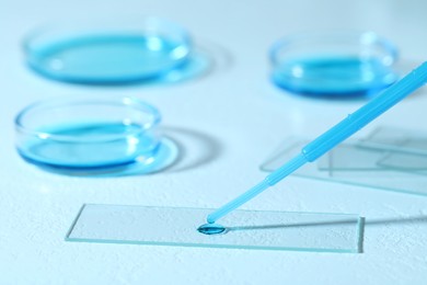 Photo of Dripping sample of light blue liquid onto microscope slide on white table