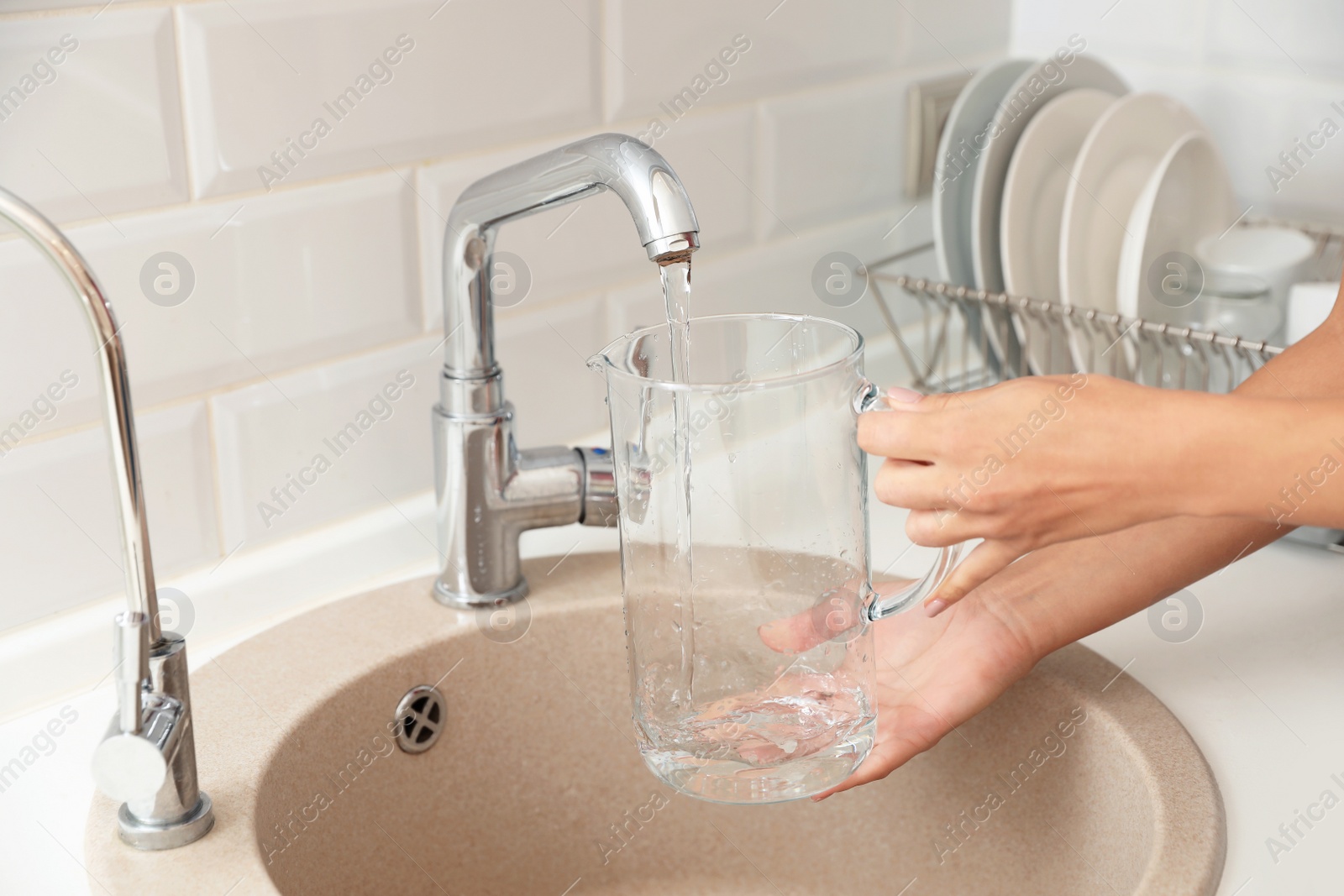 Photo of Woman pouring water into glass jug in kitchen, closeup