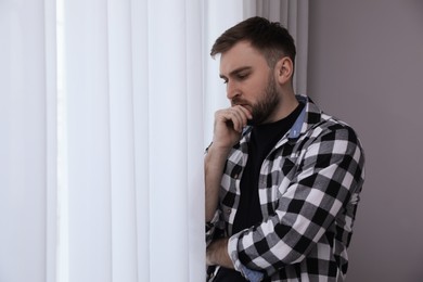 Photo of Young depressed man near window at home, space for text
