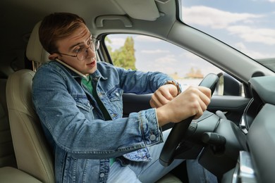 Photo of Emotional young man checking time while talking on phone in car. Being late
