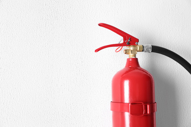 Photo of Fire extinguisher hanging on white wall, closeup. Space for text