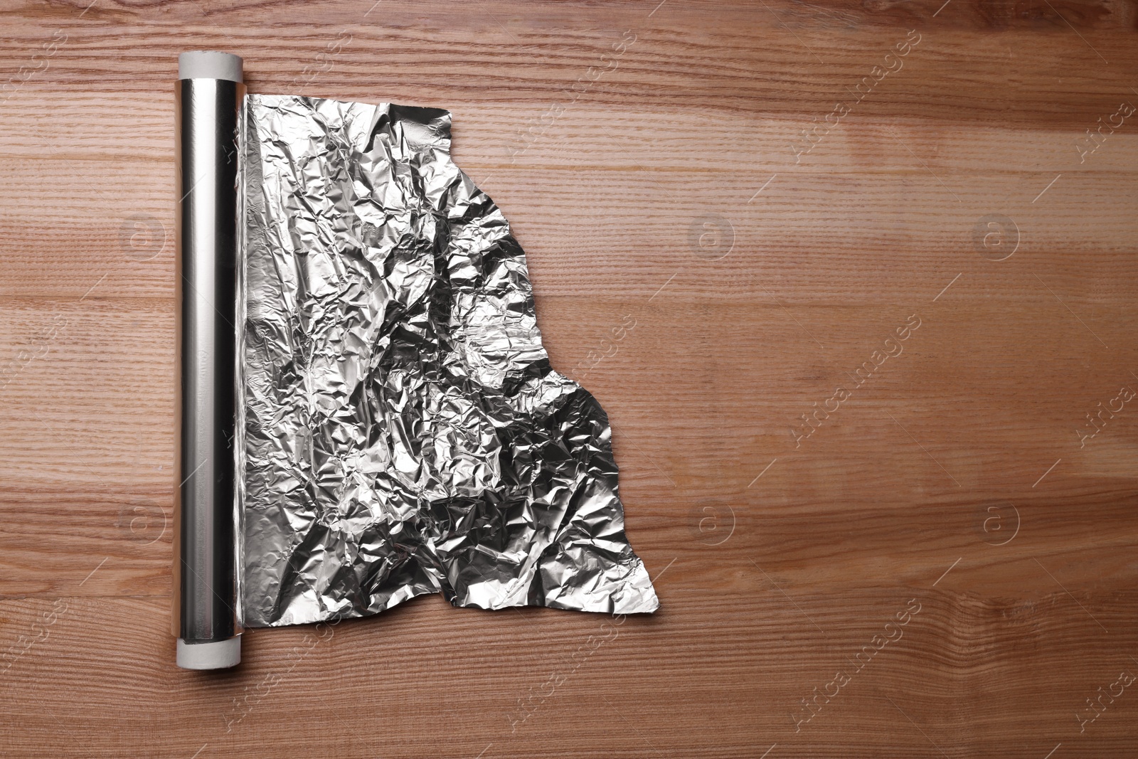 Photo of Roll of aluminum foil on wooden table, top view. Space for text