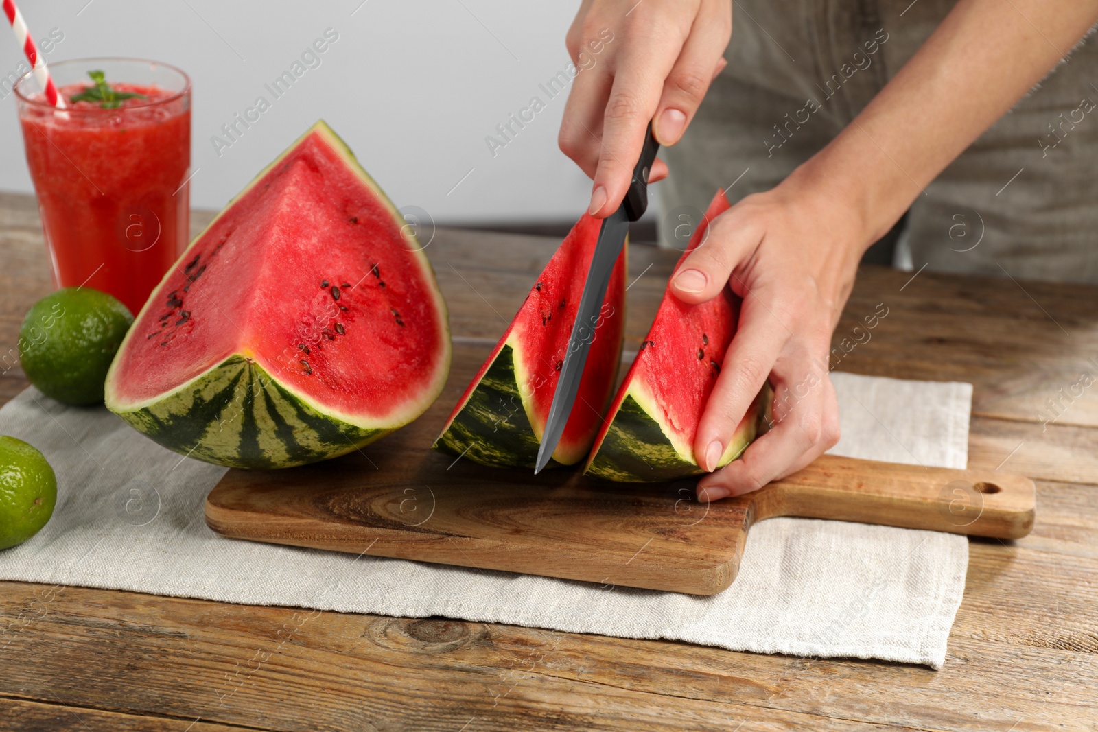 Photo of Woman cutting delicious watermelon at wooden table against light background, closeup