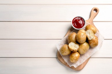 Photo of Tasty whole baked potatoes and sauce on white wooden table, top view. Space for text