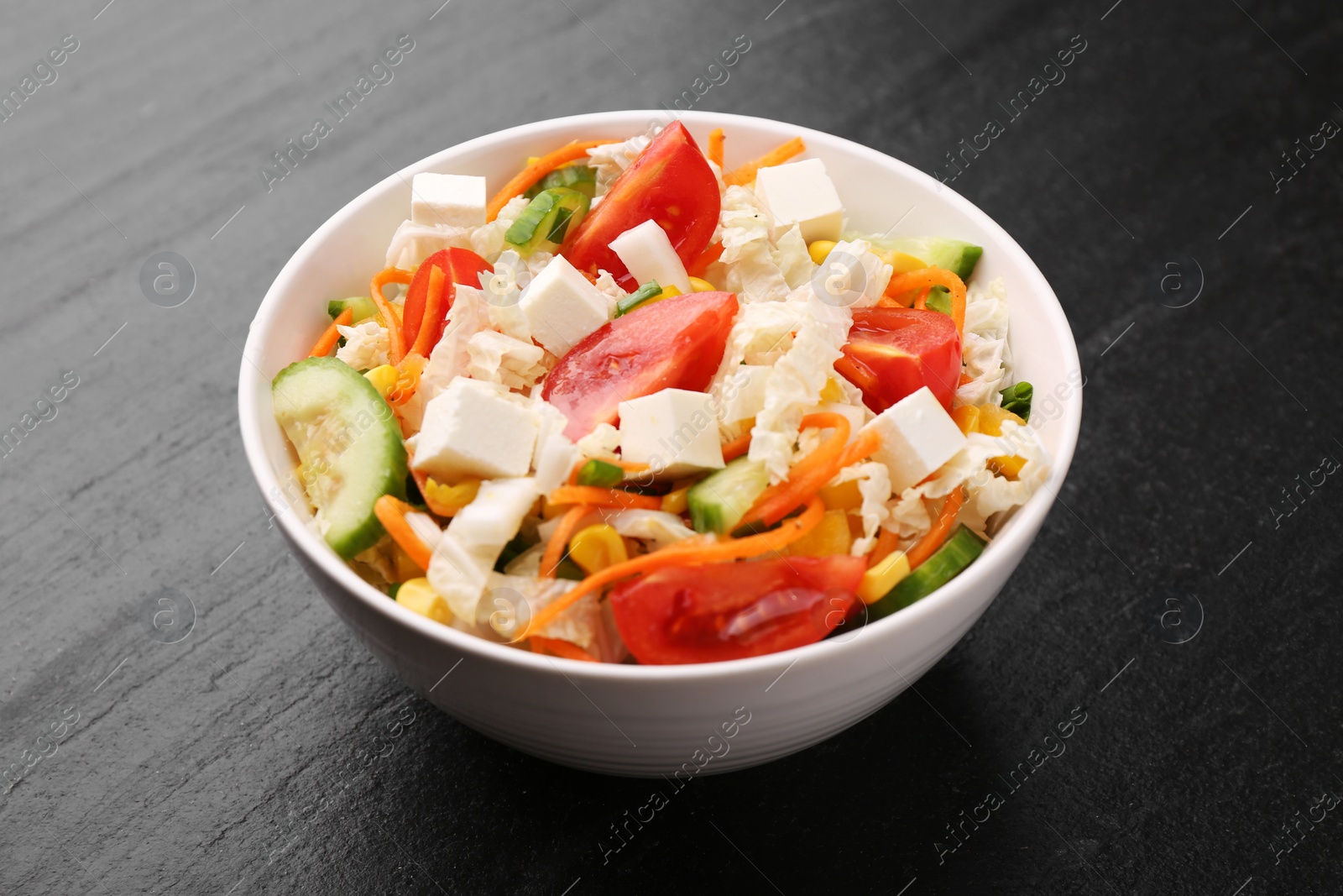 Photo of Tasty salad with Chinese cabbage, carrot, cheese, cucumber, corn and tomato on black table