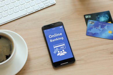 Smartphone with online banking app, credit cards and cup of coffee on wooden office table