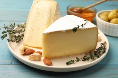 Photo of Tasty Camembert cheese with thyme and nuts on light blue wooden table, closeup