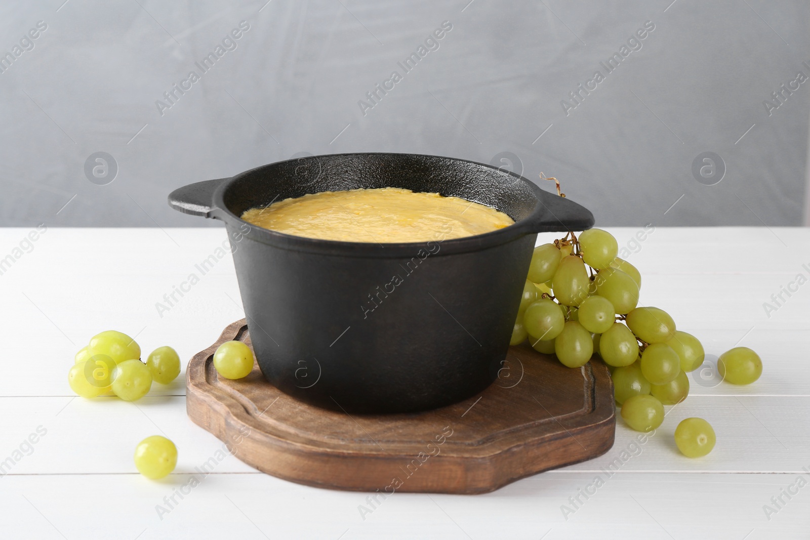 Photo of Fondue with tasty melted cheese and grapes on white wooden table